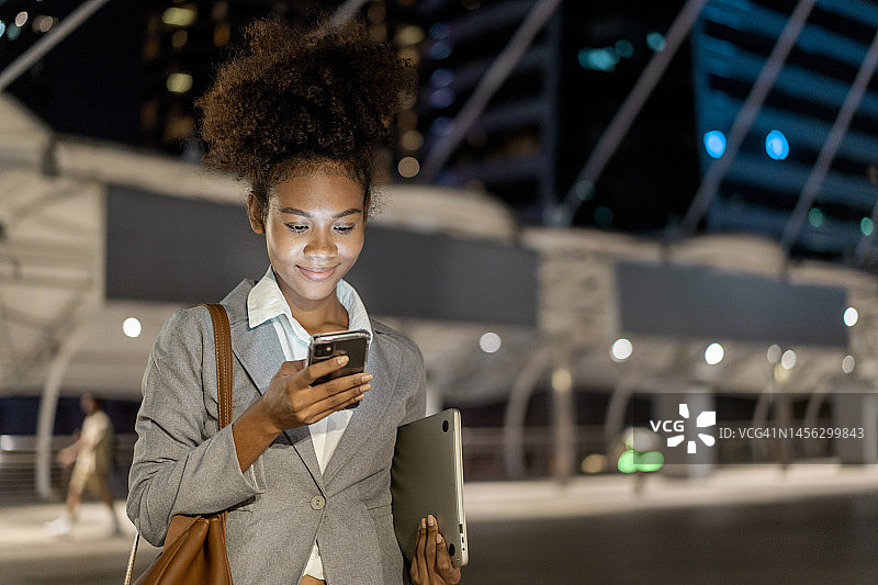 美丽的年轻女子在夜晚的城市街道上使用智能手机进行视频通话图片素材