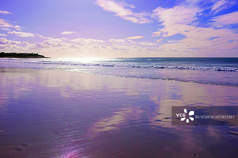 美丽的粉红色和紫色的黄昏海景在潮湿的沙滩上的倒影图片素材
