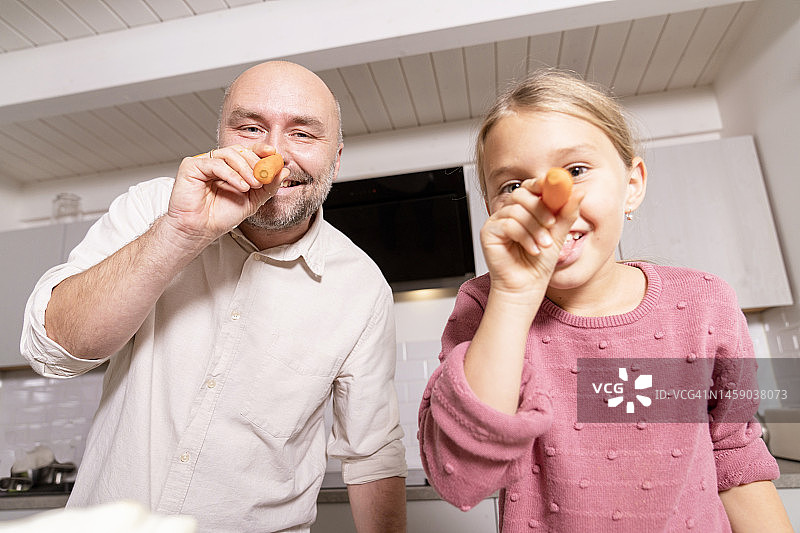 父亲和女儿在家里的厨房用胡萝卜玩得很开心图片素材
