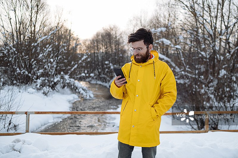 年轻人在雪天在大自然中使用智能手机图片素材