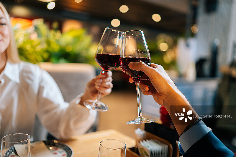 特写照片，一对相恋的情侣，晚上坐在高级餐厅的桌子前，拿着红酒碰杯。图片素材