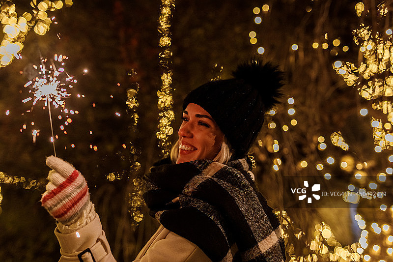 快乐的年轻女子站在闪闪发光的圣诞彩灯，挥舞着火花图片素材