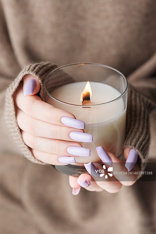 一个年轻女孩的手拿着一支蜡烛，她有着漂亮的浅紫色指甲图片素材