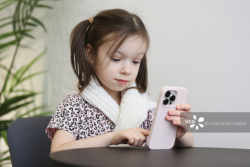 可爱的5岁女孩独自坐在咖啡馆里，使用和滚动智能手机图片素材
