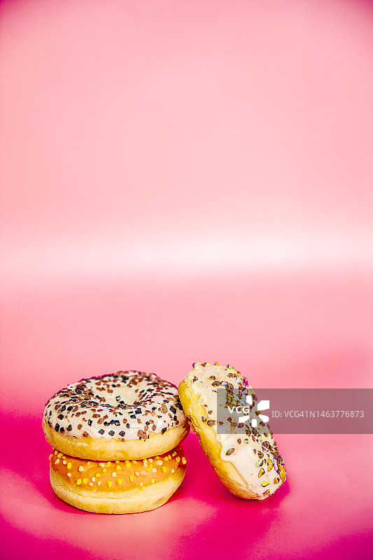 甜美的甜甜圈堆在粉红色的背景上。复制空间，各种釉料和巧克力片，零食快餐糖果概念图片素材