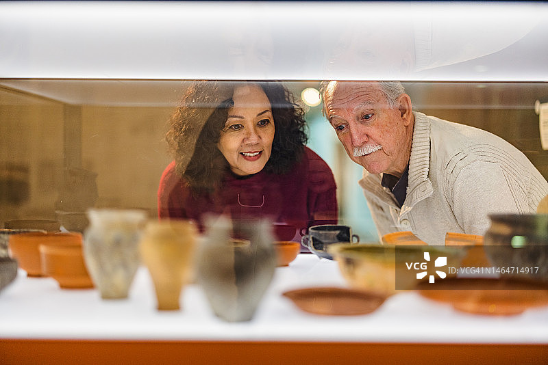 一对年长的白人夫妇正在看一个装有陶瓷器皿的玻璃陈列柜图片素材