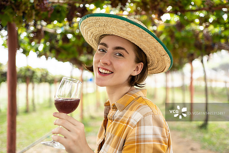 年轻快乐的白种人俄罗斯女人与绿色的眼睛品尝葡萄酒在葡萄田。快乐迷人的女性在葡萄园享受一杯葡萄酒。图片素材
