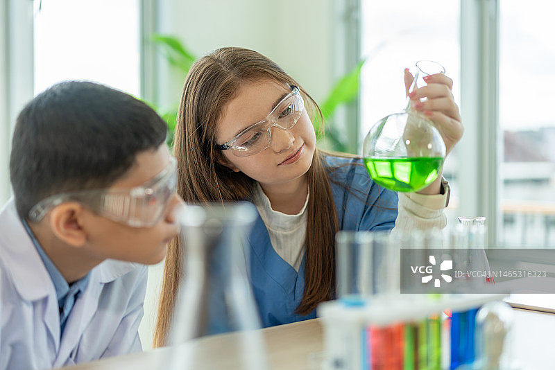 在小学科学课上，一男一女戴着防护眼镜学习化学，一边看试管。教育与科学图片素材