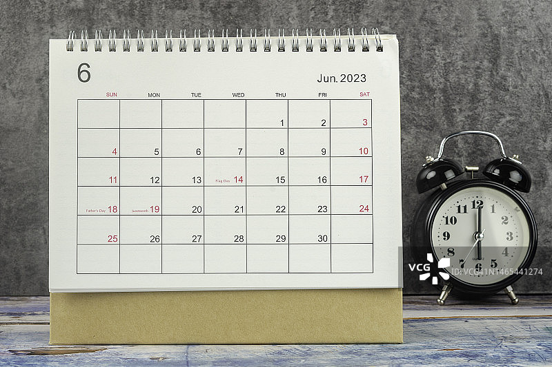 日历桌2023:六月是组织者计划和截止日期的月份，在桌子上放一个闹钟，背景是水泥。图片素材