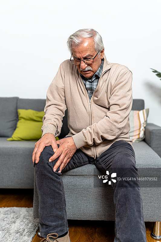 一位老人坐在家里，感到膝盖慢性疼痛，难以忍受。图片素材