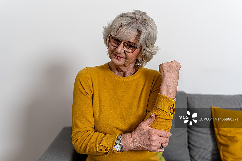 一位老年妇女坐在家里，感到肘部慢性疼痛难以忍受。图片素材