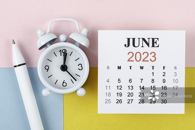 日历桌2023:六月是组织者用闹钟和白笔在双色纸背景上做计划和截止日期的月份。图片素材