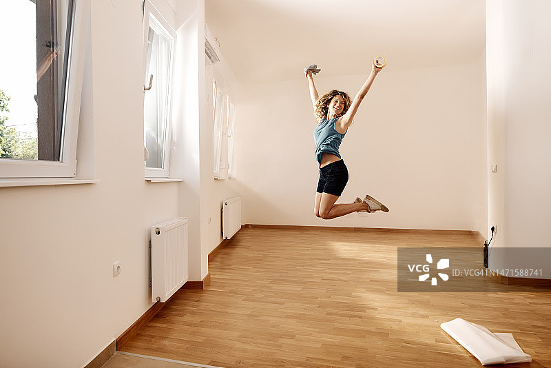 快乐的女人在她的新公寓里跳跃。图片素材