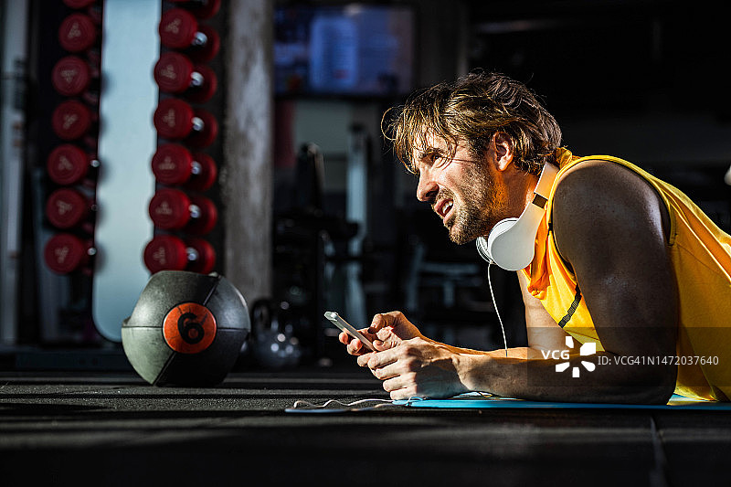 精疲力竭的运动员在健身房休息时使用手机。图片素材