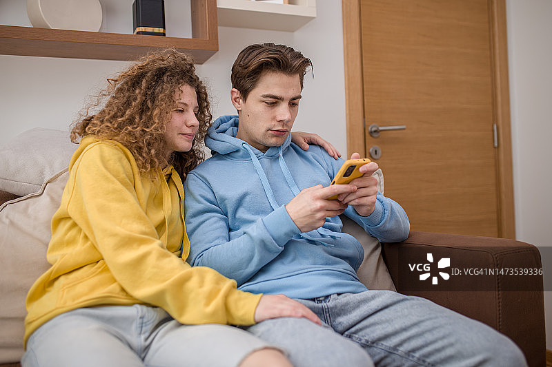 年轻幸福的夫妇看着手机，坐在客厅的科科图片素材