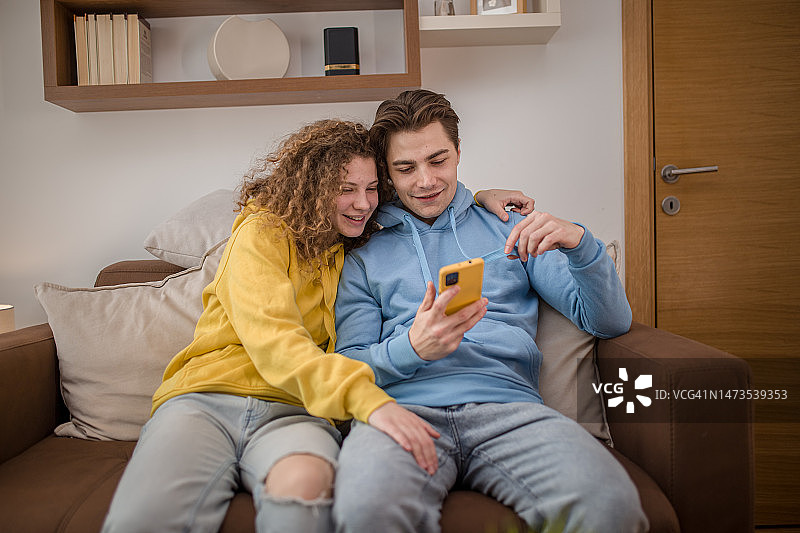 幸福的年轻夫妇坐在客厅的沙发上，用智能手机视频通话图片素材