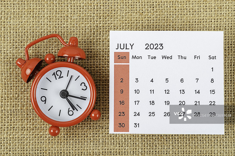 日历台2023:七月是组织者计划和截止日期的月份，在粗麻袋背景上有一个闹钟。图片素材