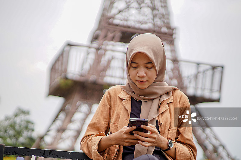 一名穆斯林女子在公园里用智能手机玩社交媒体图片素材