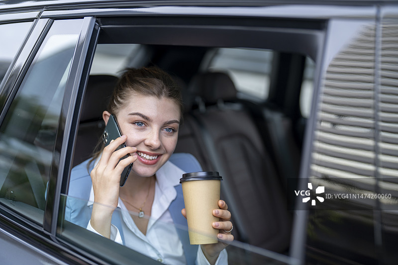 美丽的商业女性使用智能手机，微笑着坐在汽车的后座上。图片素材