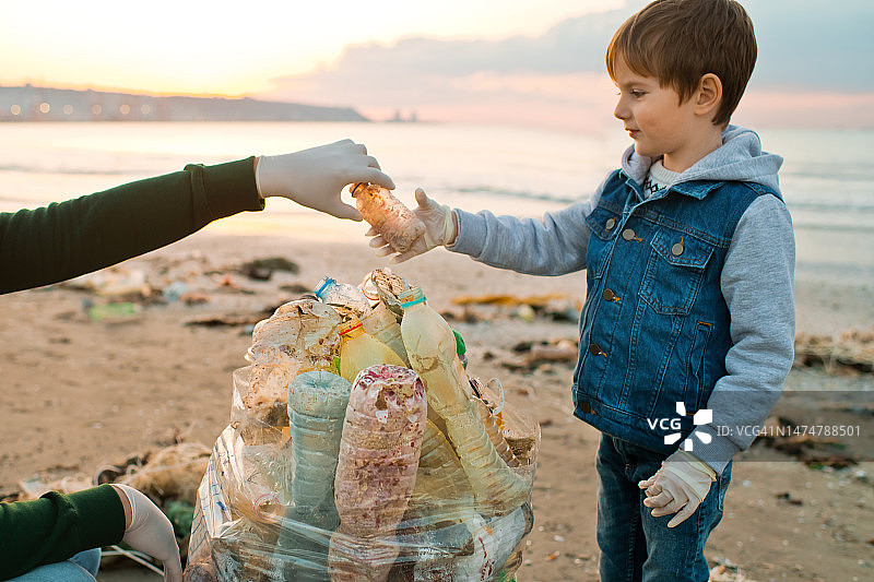 家庭志愿者通过收集废弃的塑料垃圾来清洁海滩。环境污染与生态问题概念。图片素材
