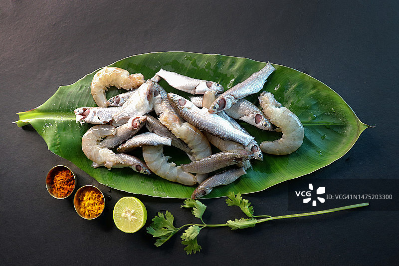印度白鲻鱼或波伊鱼和虾在绿色香蕉叶上，香料和黑色背面的烹饪材料，混合新鲜清洁的生鱼，香草和香料。副本的空间。图片素材