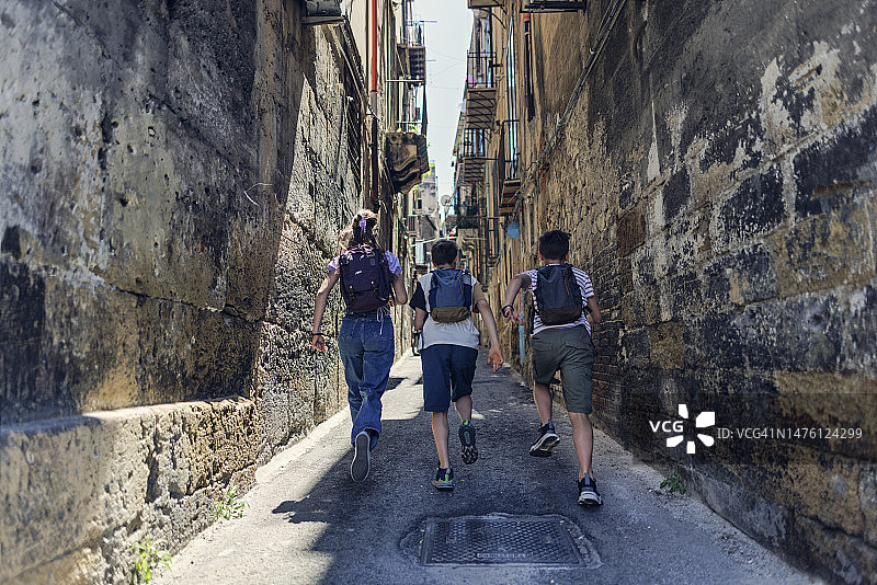 三个十几岁的孩子在意大利西西里岛巴勒莫美丽狭窄的街道上奔跑图片素材