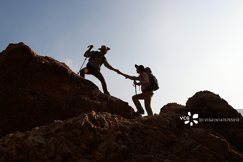 徒步队员手牵手，互相帮助，同时爬上岩石山的冒险旅行概念图片素材