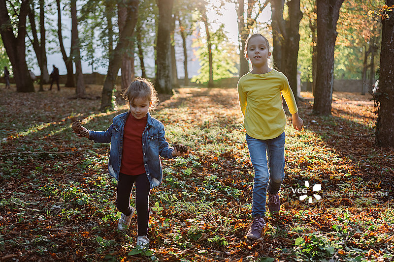 两个快乐的女孩在秋天的公园里奔跑图片素材