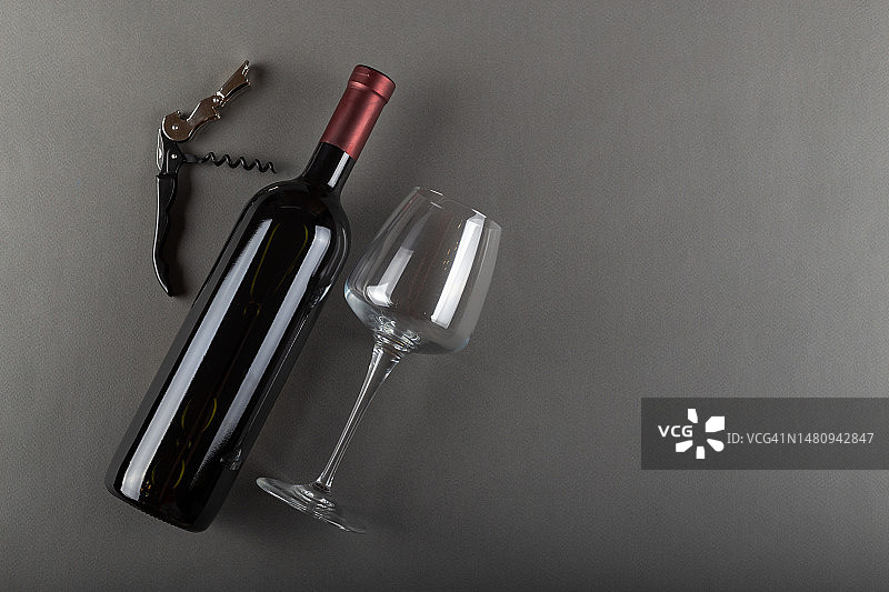 灰色背景上的红色酒瓶，开塞钻和空酒杯。酒精饮料。酿酒的概念。图片素材