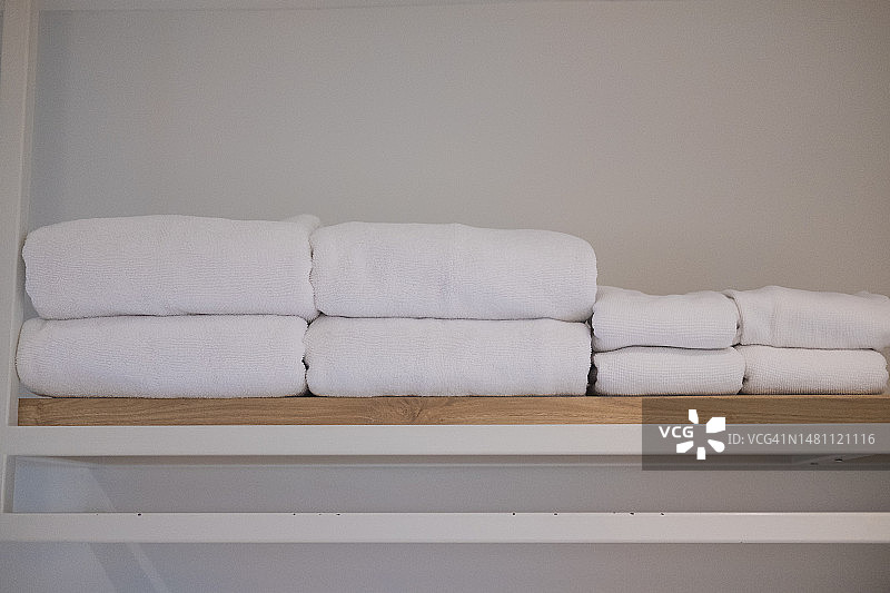 干净的白色毛巾放在木架子上，准备在酒店使用。图片素材