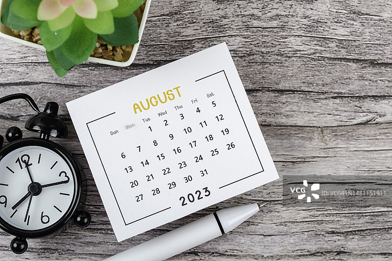 日历桌2023:8月是组织者在木桌背景上用闹钟和白笔做计划和截止日期的月份。图片素材