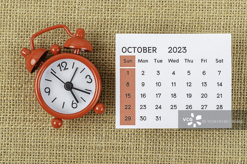 日历台2023:十月是组织者计划和截止日期的月份，在麻袋背景上有一个闹钟。图片素材