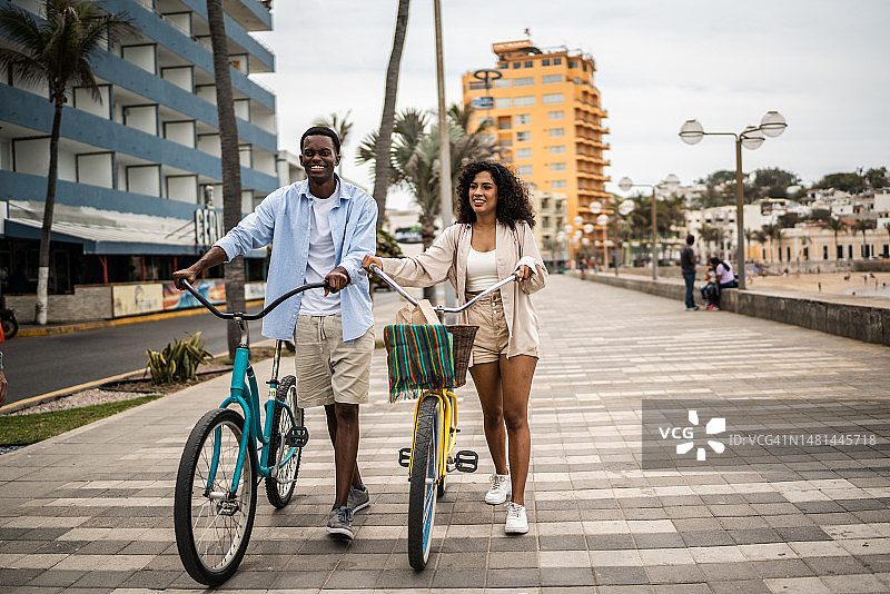 一对年轻夫妇骑着自行车在海岸线上散步图片素材