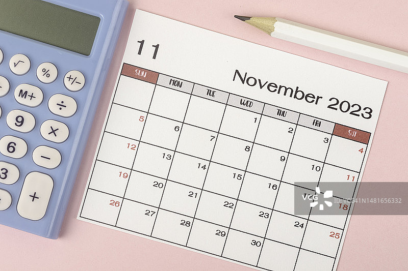 2023年日历台:11月是组织者在灰色纸张背景下，用白色铅笔和计算器来计划和截止日期的月份。图片素材