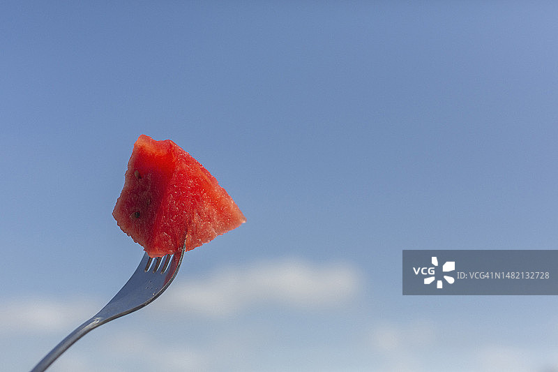 靠近叉子上多汁的红西瓜，映衬着晴朗蓝色的夏日天空图片素材