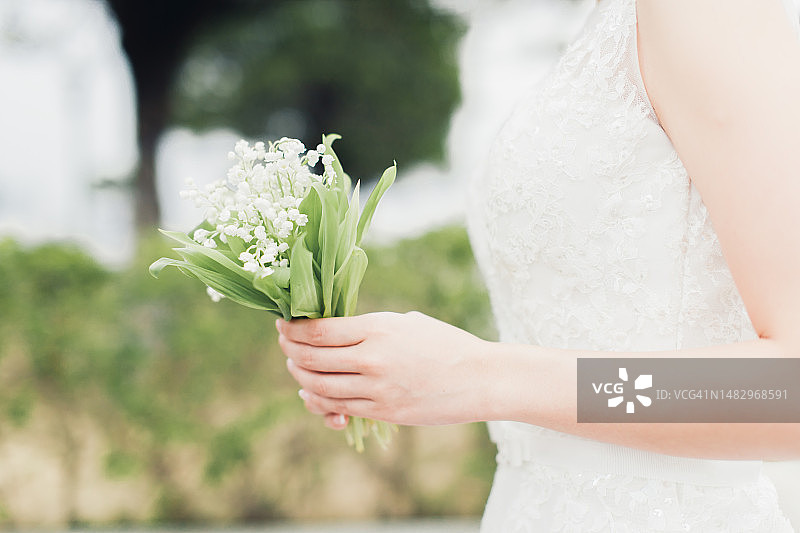 新娘手持花束站在自然公园的侧视图。婚礼的概念。图片素材
