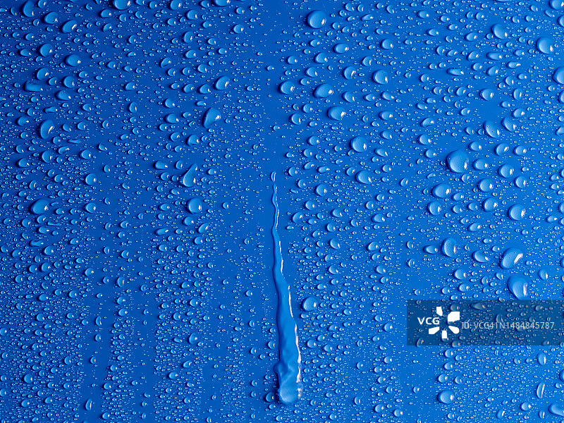 雨滴在蓝色的背景上滑落。图片素材