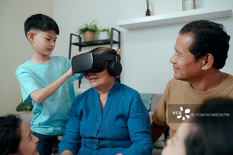 奶奶和孙子在家里玩VR头盔增强现实技术。虚拟现实的虚拟世界。图片素材