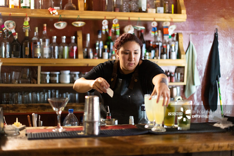 女调酒师把五颜六色的混合饮料放在吧台上，准备在餐厅供应图片素材