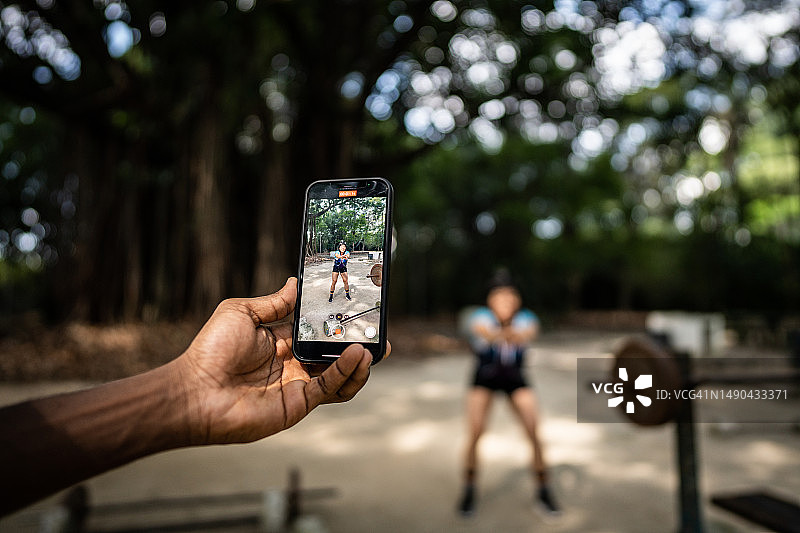 一名女性健身教练在公园里进行辅导性锻炼，被手机拍了下来图片素材