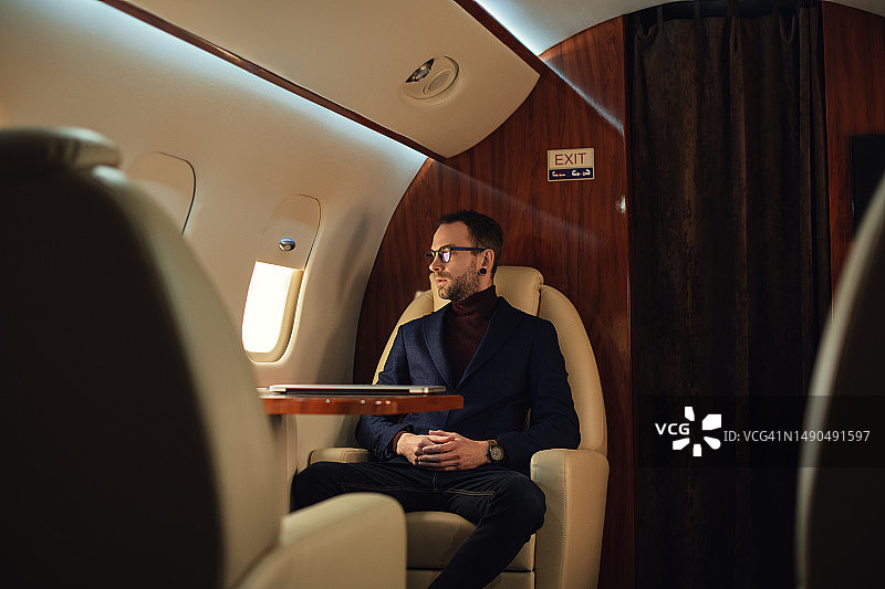 优雅的商人坐在一架私人飞机上，在起飞前透过窗户往外看图片素材