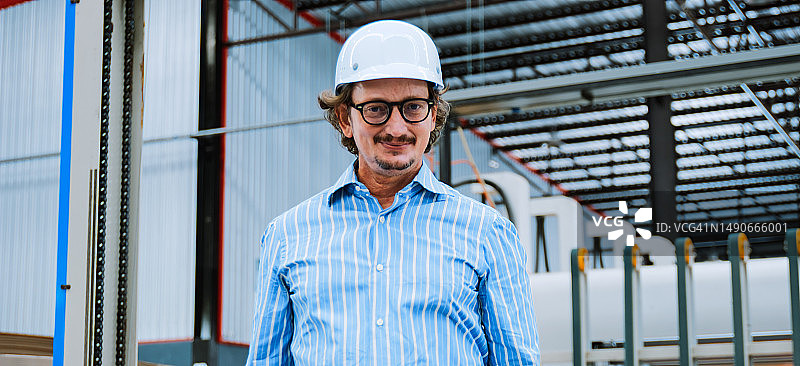 成熟的成年男性企业家商人的肖像，项目工程师经理戴着安全帽，双臂交叉在仓库包装工厂。物流行业业务，工业岗位或工作人员图片素材