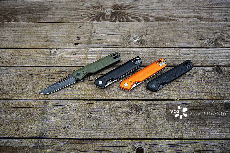 折叠不同颜色的小刀。日常携带的袖珍刀。各种刀具用于狩猎、运动和娱乐。木制背景。图片素材