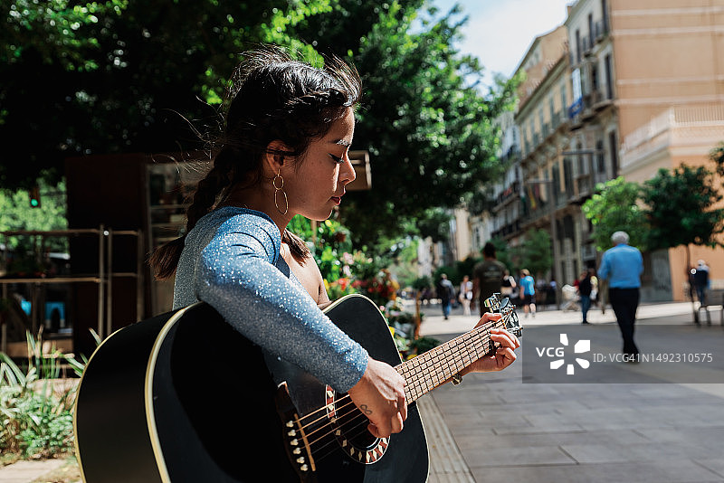 一个南美女人坐在城市的长椅上弹吉他的画像。图片素材