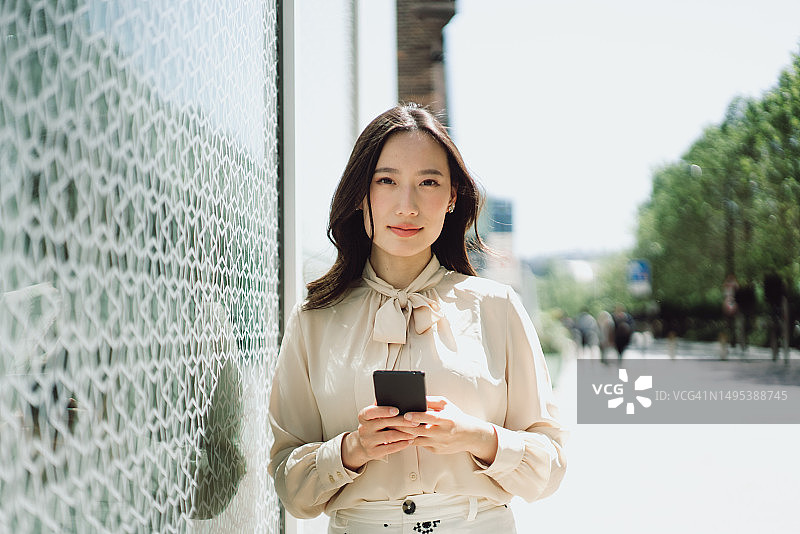 一个漂亮的亚洲女人在街上用智能手机的照片。图片素材
