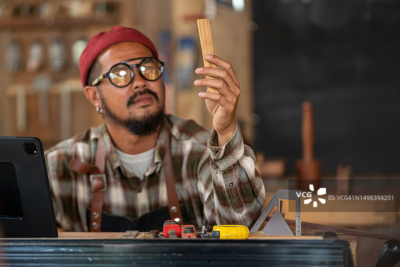 专业木匠坐在桌子上，通过平板电脑展示木制物品，同时在线视频聊天。图片素材