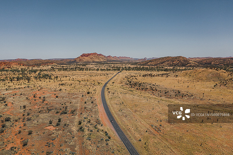 航拍照片显示，在一个阳光明媚的日子里，一辆汽车在偏远的柏油路上驶向山区，澳大利亚北部地区图片素材