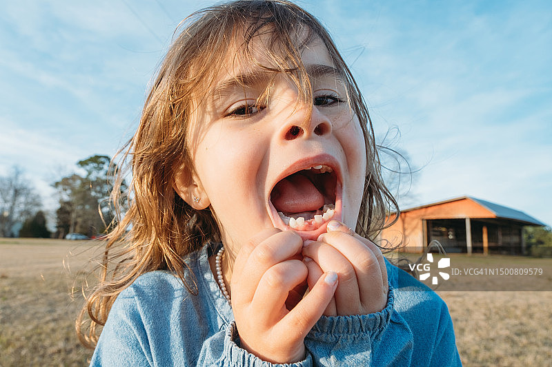 可爱的小女孩骄傲地张开嘴，展示她掉的第一颗牙。图片素材