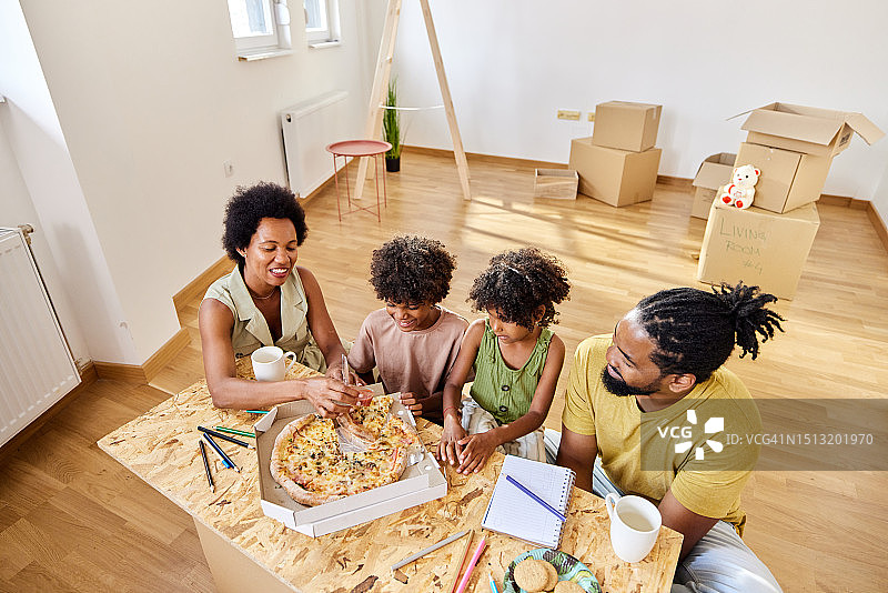 快乐的黑人家庭在新家打开行李后吃着披萨。图片素材