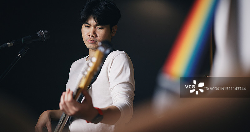 穿着便服的年轻亚洲男音乐家在灯光明亮的工作室里弹着电吉他排练图片素材